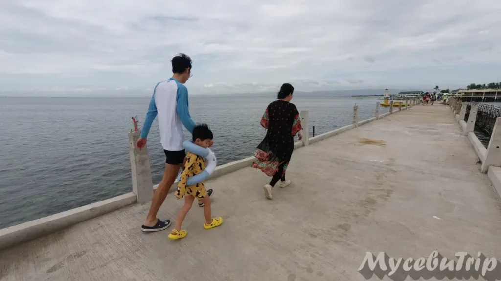 A family walking on the long pier at Nalusuan Island under a cloudy sky during a Cebu hopping tour.