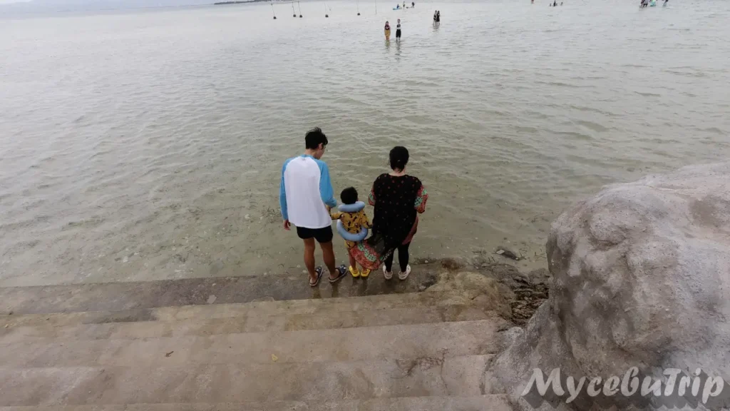 Family standing by the shallow waters and sandbar behind Nalusuan Island