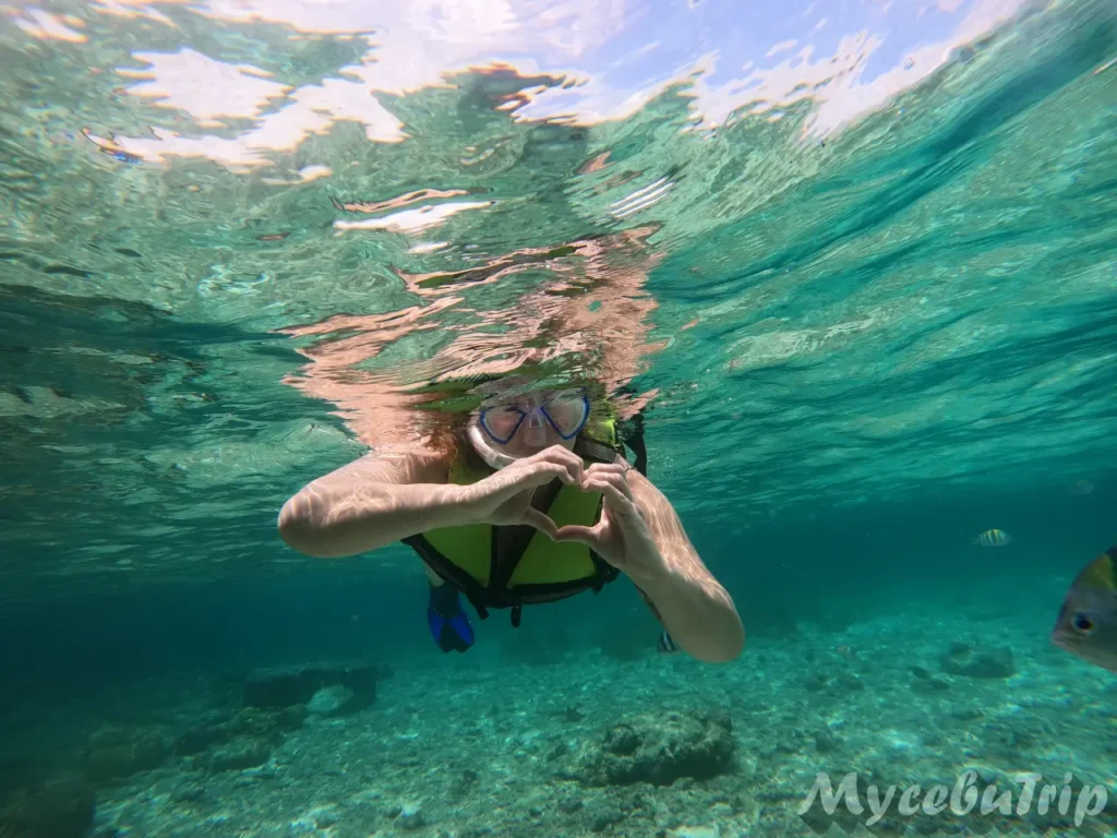 Snorkeler in a life vest making a heart sign underwater at Nalusuan Marine Sanctuary